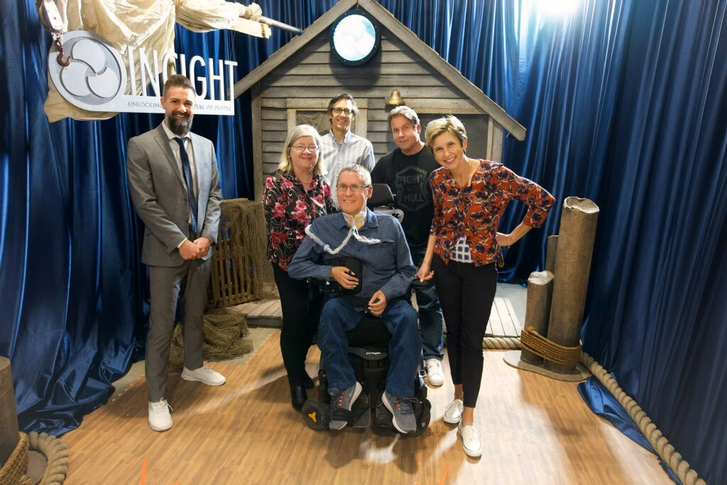 The INCIGHT team of six standing together in front of a nautical-themed set, Scott Hatley seated in his wheelchair at the center.