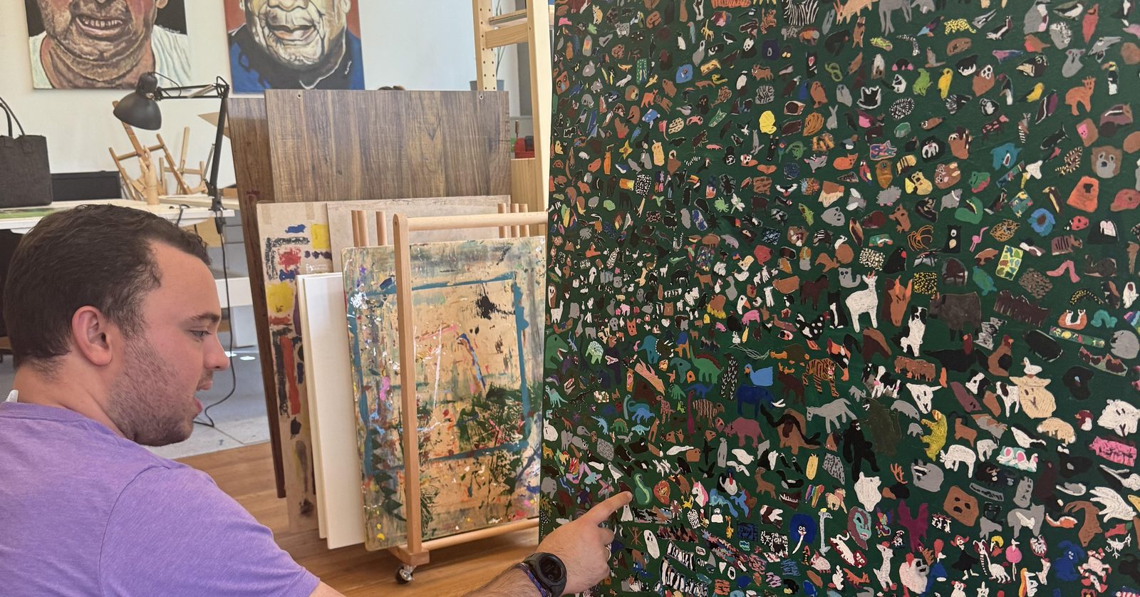 Davis Wohlford at North Pole Studio, pointing out detail on a large animal painting.